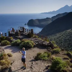 Un hombre toma una foto desde el mirador Cabo de Gata, con el mar azul y montañas al fondo.