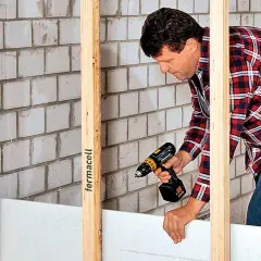 Mann baut eine Trockenbauwand mit Akkuschrauber und Gipskartonplatten.
