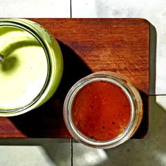 Zwei Gläser mit Saucen: ein cremiges Avocado Dressing für Salat und eine rote Vinaigrette.