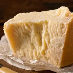 Un pezzo di formaggio stagionato, ideale per chi cerca un formaggio senza lattosio, su carta da forno con un coltello.