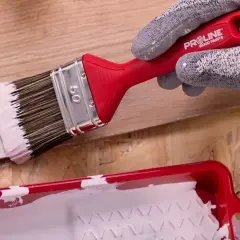 Ręka w rękawicy maluje drewno białym pędzlem. Różne rodzaje pędzli malarskich pomagają w precyzyjnym malowaniu.
