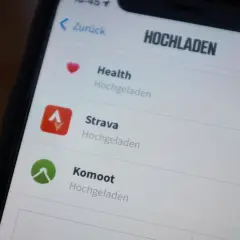 Na ekranie telefonu widać aplikację Strava, obok niej ikonę "Hochgeladen".