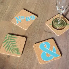 Vier bemalte Bierdeckel mit Farnblatt, Ampersand und "Nº 89" in Blau und Grün auf Holz.