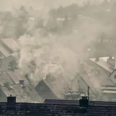 Dym wydobywający się z kominów domów na tle mglistego krajobrazu.