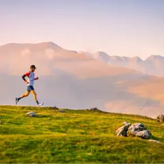Un coureur en plein effort sur un sentier de montagne, profitant d'un paysage spectaculaire au lever du soleil.