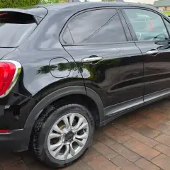 Czarny Fiat 500X widziany z boku, na brukowanym podjeździe.
