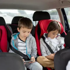 Im Auto mit 3 Kindern: Ein Baby schläft, die älteren Brüder sind mit ihren Handys beschäftigt.