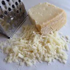 Tarty kawałek Grana Padano i świeżo starty ser obok tarki. Wskazówka, jak przechowywać Grana Padano, aby zachował świeżość.