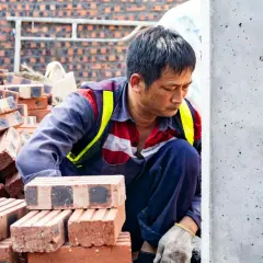 Budowlaniec w kamizelce odblaskowej pochyla się nad stertą cegieł. Czyżby obawiał się, że murowanie przerwą nocne przymrozki?