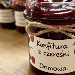 Słoik z domową konfiturą z czereśni, ozdobiony sznurkiem i etykietą z rysunkiem owoców.