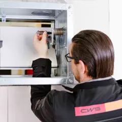 Techniker prüft die brandschutzklappe funktion. Er justiert eine Feder im Metallgehäuse, um die Sicherheit zu gewährleisten.