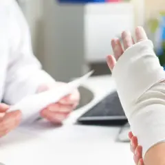 Lekarz bada rękę z opatrunkiem, zastanawiając się, czy wybity palec puchnie.