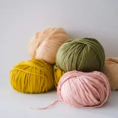 Pelotes de laine aux couleurs pastel, dont une rose pâle, une verte et une jaune. La matière semble être du nylon, parfaite pour des créations durables.