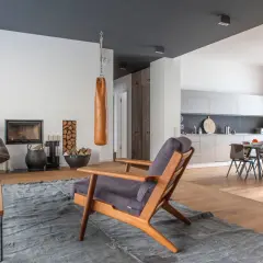 Ein Wohnzimmer mit Kamin, Ledersessel und einem Holzstuhl. Die Kombination von Holzarten im Boden und Möbeln schafft eine warme Atmosphäre.