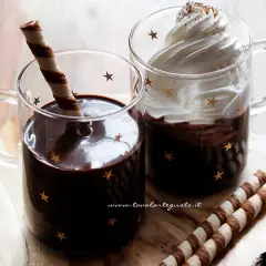 Due tazze di cioccolata calda con cacao e latte, una con panna e cacao, l'altra con un biscotto.