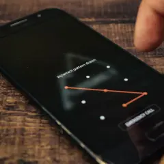 Palec próbuje odblokować telefon, wpisując błędny wzór. Ekran pokazuje komunikat "Incorrect pattern drawn" i opcję "EMERGENCY CALL".