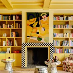 Ein Wohnzimmer in einem gelben Farb-Drenching-Stil mit Bücherregalen, einem Kamin und einem bunten Sofa.