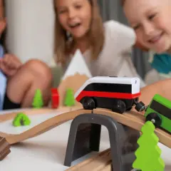 Dzieci bawią się drewnianym pociągiem na torach. Radość na ich twarzach podczas zabawy.