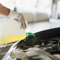 Rękawiczki i kanister z żółtym płynem. Mechanik uzupełnia płyn chłodniczy G12++, co oznacza jego wysoką jakość i ochronę silnika.