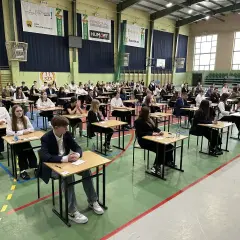 Uczniowie siedzą przy ławkach w sali gimnastycznej, skupieni na zadaniach. To ważny dzień, kiedy egzamin ósmoklasisty.