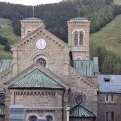 Bazylika Matki Bożej z La Salette, kamienna budowla z wieżami i zegarem, wznosi się na tle zielonych górskich zboczy.