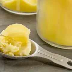 Łyżka masła klarowanego, które jest tematem dyskusji, czy masło klarowane jest zdrowe. Obok słoik z tym tłuszczem.