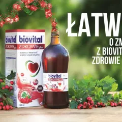 Biovital Zdrowie Plus – suplement diety z głogiem i witaminami. Pudełko i butelka na drewnianym stole, otoczone gałązkami z czerwonymi owocami.