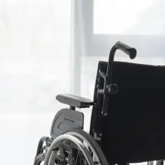 Czarne siedzisko wózka inwalidzkiego na tle jasnego okna.