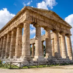 Ancient Greek temple ruins, a highlight of a 2 week Sicily itinerary, stand majestically under a blue, cloudy sky.