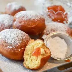 Rosquillas de naranja recién hechas, espolvoreadas con azúcar glas. Una está partida, mostrando su relleno de mermelada.