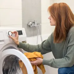 Frau stellt Waschmaschine ein, um den Wasserverbrauch zu optimieren. Sie hält ein gelbes Kleidungsstück in der Hand.
