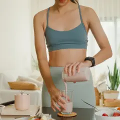 Frau mixt einen Smoothie, der zeigt, wie Proteinpulver beim Abnehmen helfen kann. Gesunde Zutaten liegen bereit.