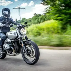 Motocyklista w kasku i kurtce jedzie drogą. Kask i kurtka to obowiązkowe wyposażenie motocykla, zapewniające bezpieczeństwo.