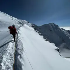 Bergsteiger auf dem Weg zum Mont Blanc besteigen, gesichert durch ein Seil, mit atemberaubendem Blick auf schneebedeckte Gipfel und Wolkenmeer.