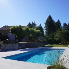 Belle propriété avec piscine, un projet de création bassin réussi. La maison en pierre et les arbres créent un cadre idyllique.