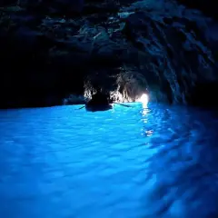 Barca a remi naviga nelle acque azzurre della grotta dello smeraldo, illuminata dalla luce che filtra dall'esterno.