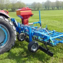 Tracteur rouge avec semoir bleu pour le sursemis de prairie. L'outil prépare le sol avant de semer de nouvelles herbes.
