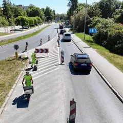 Prace drogowe na linii 101 w Szczecinie. Robotnicy w kamizelkach odblaskowych układają nawierzchnię, jeden z nich pcha taczkę z materiałem.