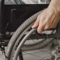 Dłoń osoby w dżinsach trzymająca obręcz koła wózka inwalidzkiego.