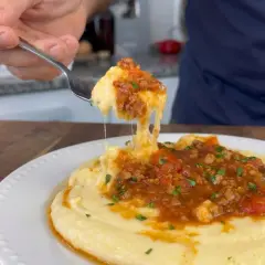 Un tenedor levanta una porción de polenta con tuco, mostrando su textura cremosa y la rica salsa de carne y tomate.