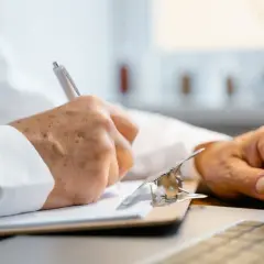 Doktor nauk medycznych w białym kitlu notuje informacje na kartce.