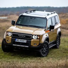 Złoty Toyota Land Cruiser z czarnymi dodatkami i relingami dachowymi stoi na trawiastym wzgórzu.