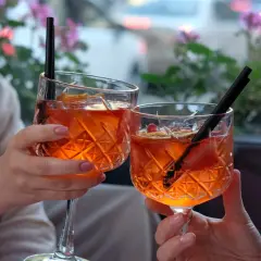 Dwie osoby wznoszą toasty Aperolem bezalkoholowym. Przepis na ten orzeźwiający drink jest prosty, a efekt zachwyca.