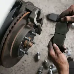 Mechanik trzyma zużyte klocki hamulcowe, zastanawiając się, co ile wymieniać klocki hamulcowe. W tle widać tarczę hamulcową.