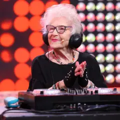 DJ Wika w słuchawkach, z uśmiechem na twarzy, miksuje muzykę. W tle czerwone i białe światła.