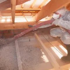 Persona in tuta protettiva insuffla materiale isolante in un sottotetto non abitabile, un progetto fai da te per migliorare l'efficienza energetica.