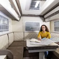 Aménagement du camping car salon arrière : une femme prépare son itinéraire sur une carte.
