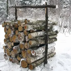 Stos drewna, prawdopodobnie metr sześcienny, przygotowany do zimowego ogrzewania. Kłody pokryte śniegiem, otoczone zimowym lasem.