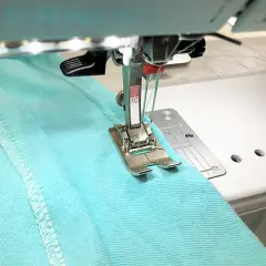 A double needle stitches a hem on turquoise fabric. Most sewing machines can use a double needle with the right setup.