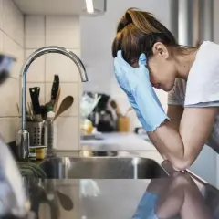Kobieta w rękawiczkach opiera się o zlew, wyraźnie przygnębiona. Mizofobia utrudnia jej codzienne czynności.